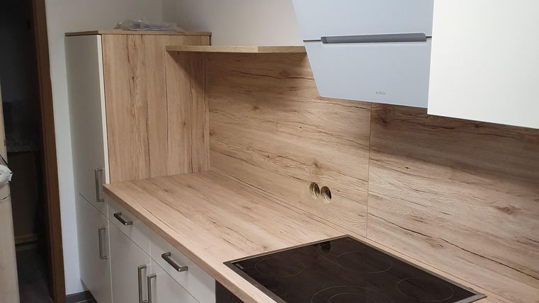 A modern kitchen with wood and white fronts. It features a cooktop, an oven, and ample storage space.