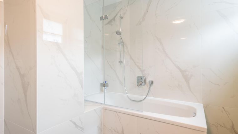 Ein modernes Badezimmer mit einer Badewanne und eleganten, marmorierten Wänden. Das helle Licht sorgt für eine einladende Atmosphäre.