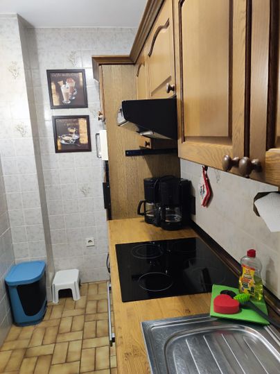 A cozy kitchen with wooden cabinets and a stove. On the countertop, there is a coffee machine and kitchen utensils.