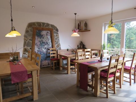 A cozy restaurant with wooden tables and chairs. The large window front lets in plenty of light and offers a view of the greenery.