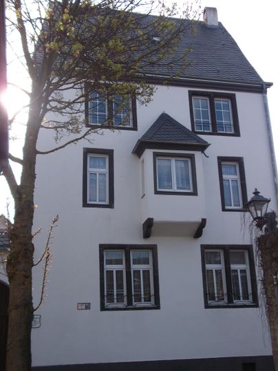 A three-story, white building with a pointed roof. It has several windows and is next to a tree.
