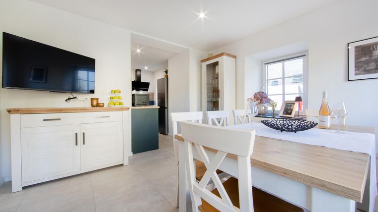 Eine moderne Küche mit einem Esstisch und einem großen Fernseher an der Wand. Die Atmosphäre ist hell und freundlich.