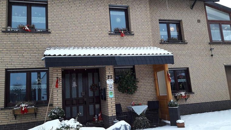 Une maison enneigée avec une entrée accueillante. Les fenêtres sont décorées pour les fêtes et la zone est joliment ornée.