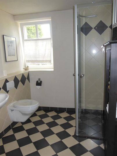 Ein modernes Badezimmer mit einer Dusche und einem WC. Der Boden ist in einem schwarz-weißen Schachbrettmuster gestaltet.
