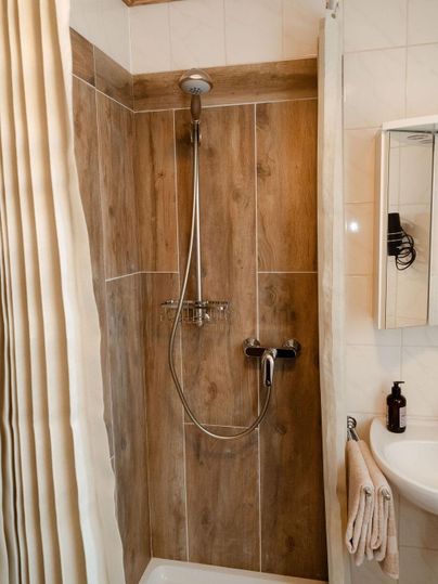 Une douche moderne avec un aspect bois et des carreaux blancs. Il y a une douche, un porte-serviettes et un miroir.