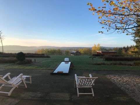 Een rustige terras met twee ligstoelen en een lange, spiegelende waterpartij. Op de achtergrond strekt zich een groene landschap onder een heldere lucht uit.