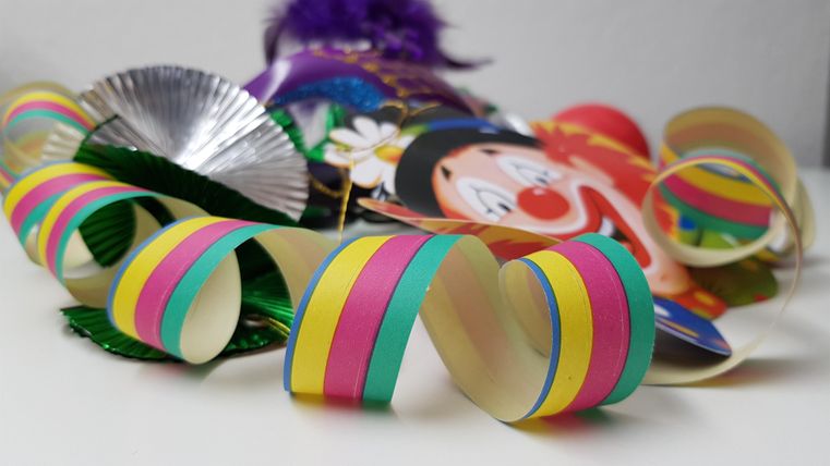 Colorful decorations for a celebration, including a clown mask and wavy ribbons. The colors are vibrant and festively designed.