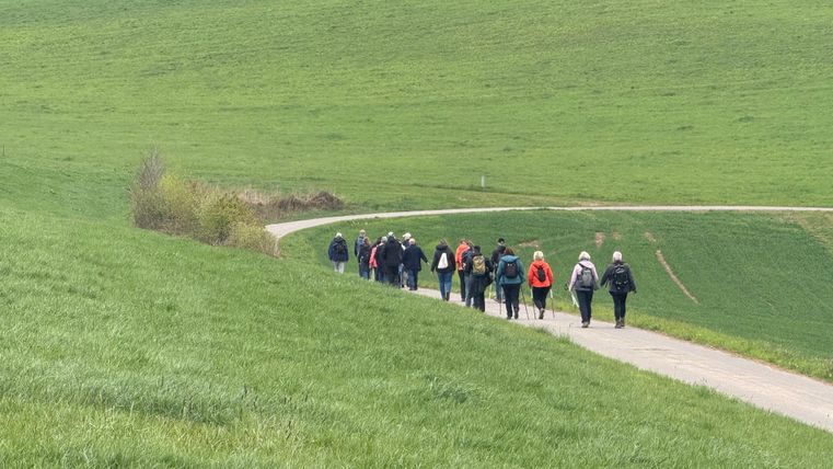 Een uitgestrekt landschap met groene weiden en een heldere blauwe lucht. Op de voorgrond staat een groot kruis.