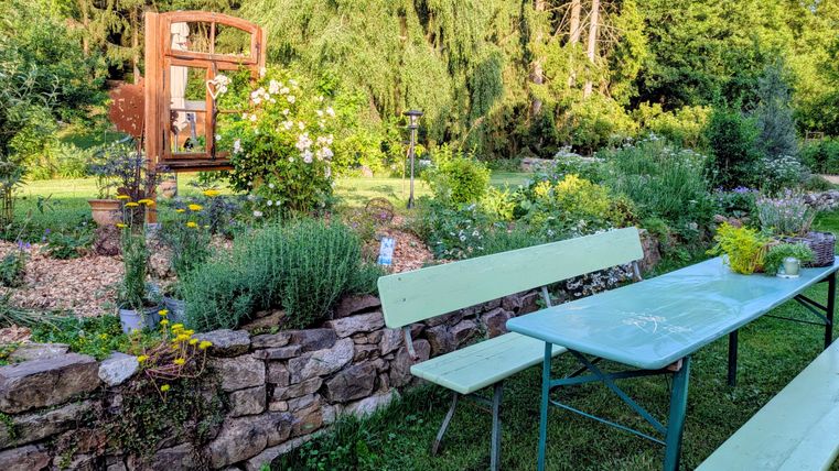 Ein schöner Garten mit einer Steinmauer und bunten Blumen. Ein Tisch und Bänke laden zum Entspannen ein.