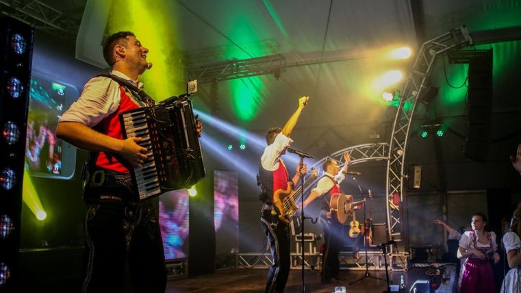 Een band speelt op een podium met kleurige lichten. Muzikanten met een accordeon en een gitaar zorgen voor een goede sfeer.