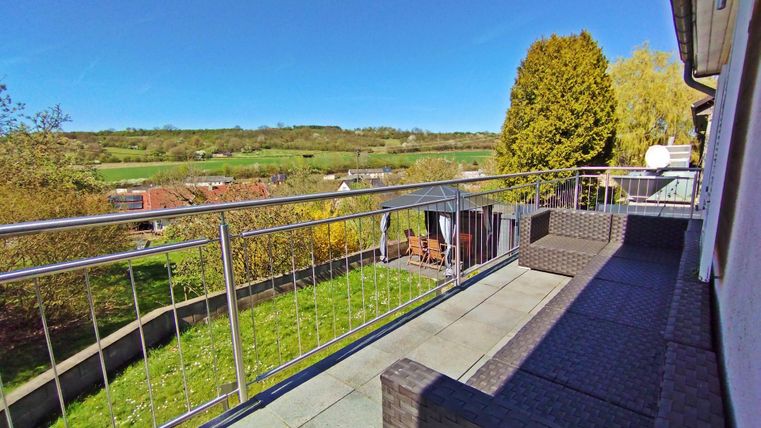 Un joli balcon avec une vue sur des prairies vertes et des arbres. La terrasse est équipée de meubles modernes.