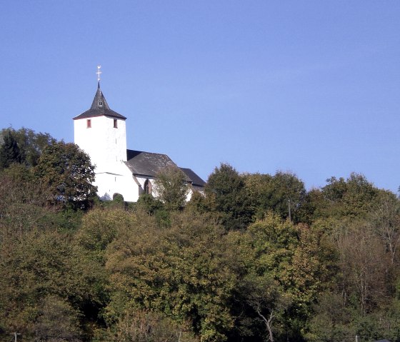 De oude kerk St. Apollonia in Gransdorf troont op een beboste heuvel onder een helderblauwe hemel., © Doris Pauels