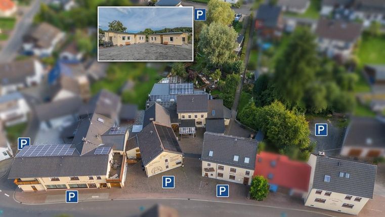 Een luchtfoto van meerdere gebouwen met parkeerplaatsen. In het bovenste gedeelte is een afbeelding van een groter bouwproject te zien.