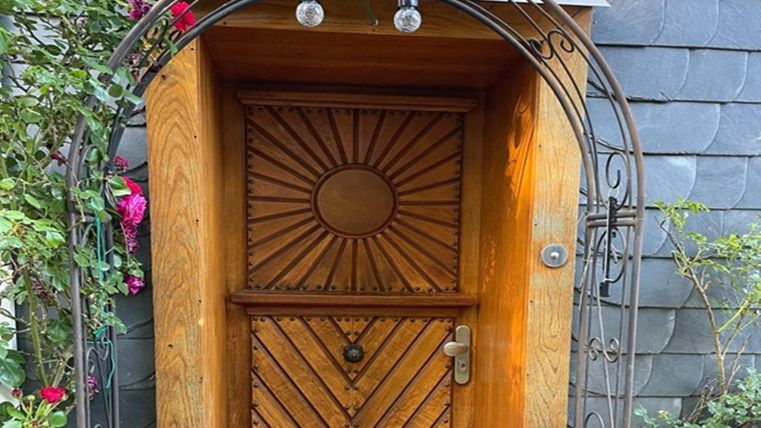 A beautiful wooden front door with a decorative pattern. The door is surrounded by a metal arch and plants.
