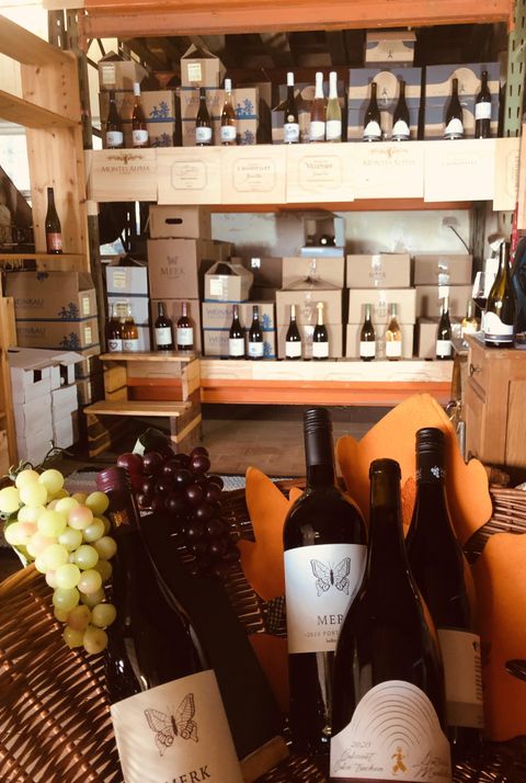 A wine shop with several shelves filled with wine bottles. In the foreground are some wine bottles and grapes.