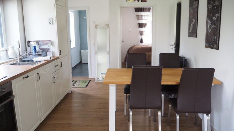 Eine helle Küche mit einem Esstisch und vier Stühlen. Der Raum ist modern eingerichtet und hat große Fenster.