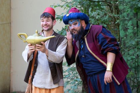 Deux hommes en vêtements fantasques se tiennent dans un environnement verdoyant. L'un tient une lampe en or et ils semblent surpris ou ravis.