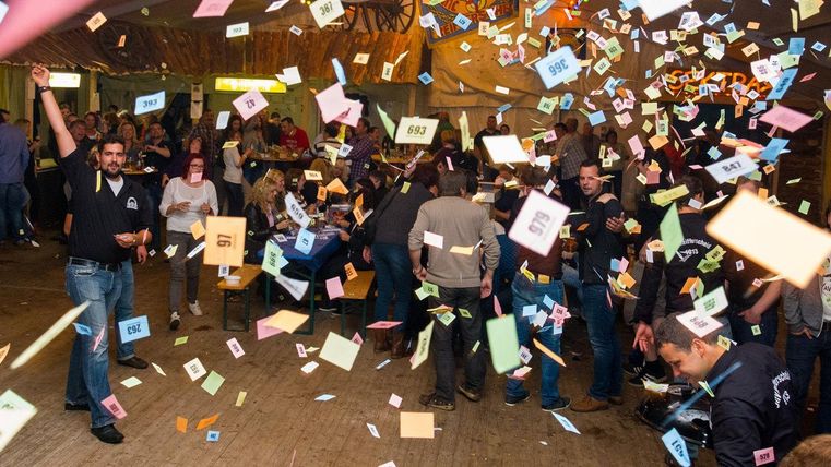 Een levendig feest in een zaal vol mensen. Kleurrijke stukjes papier vliegen door de lucht en er heerst een vrolijke sfeer.