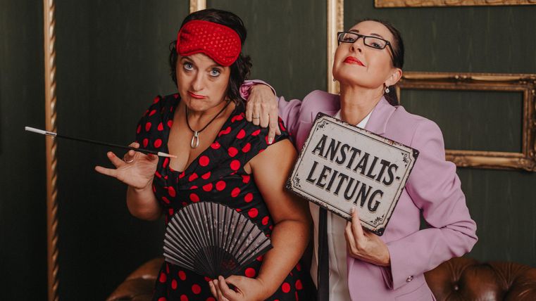 Two women pose humorously; one holds a sign that says "Institution Management".