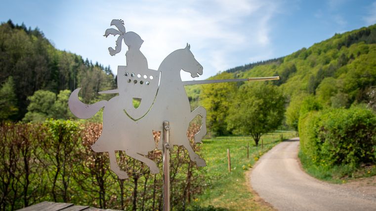 Metalen figuur van een ridder op een paard voor een groen landschap.