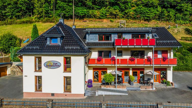 Een charmant hotel met rode balkons in een groene omgeving. De gevel ziet er uitnodigend en vriendelijk uit.