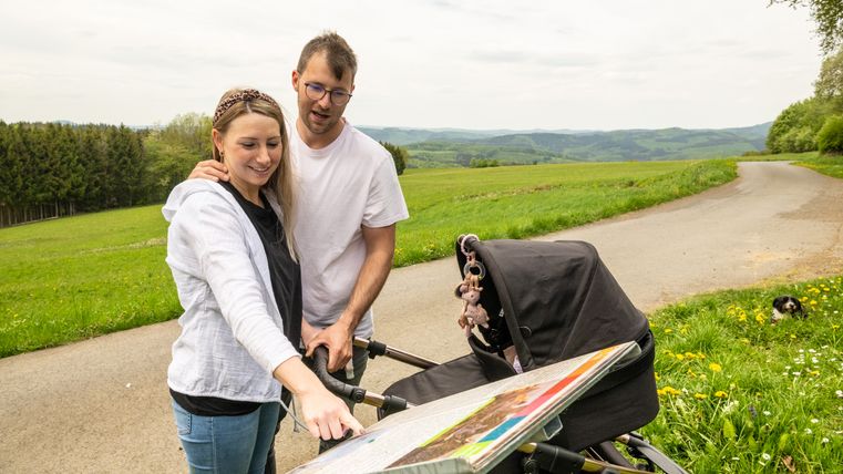 Een stel met een kinderwagen bekijkt een kaart in een landelijke omgeving.