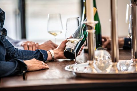 Une table élégante avec des verres et une bouteille de vin. Des mains de personnes sont visibles alors qu'elles versent le vin.