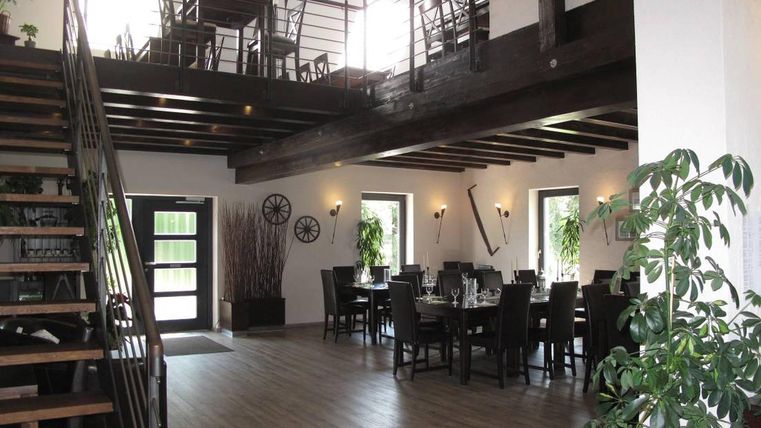 Modern barn with wooden beams, staircase, dining tables, and plants. Bright windows and stylish decoration.
