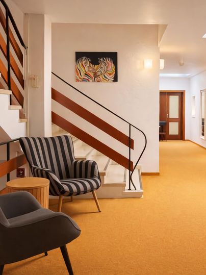 Ein modern eingerichteter Flur mit einer Treppe und einem gemütlichen Sessel. An der Wand hängt ein farbenfrohes Kunstwerk.