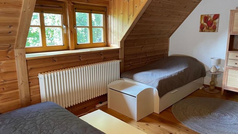 A cozy bedroom with wooden paneling and two single beds. There are windows with a view of the greenery and a round rug on the floor.