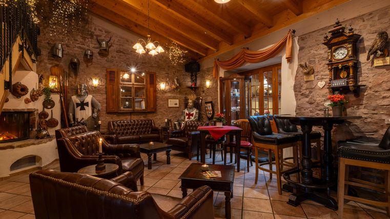 Een gezellig restaurant met leren stoelen en een houten plafond. Aan de muren hangen decoraties en een oude klok, terwijl een raam licht de ruimte binnenlaat.