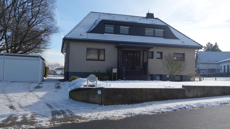 A large house in the snow with a clear sky. The driveway is covered in snow and the surroundings are quiet.