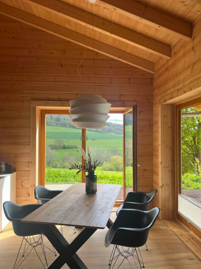 Ein moderner Essbereich mit einem Holztisch und eleganten Stühlen. Große Fenster bieten einen Blick auf die grüne Landschaft.