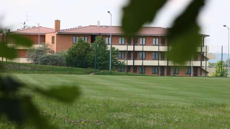A modern building with several floors stands in a green landscape. Surrounded by meadows and trees, it appears inviting and tranquil.