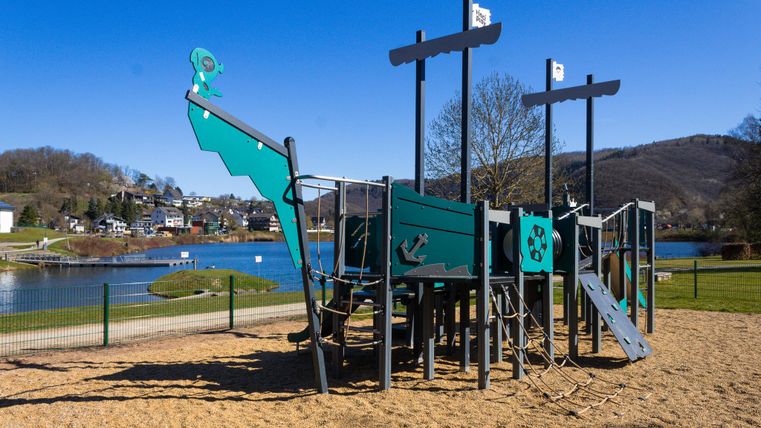 A quiet park with a pond and green grass. In the background, trees and gentle hills can be seen.