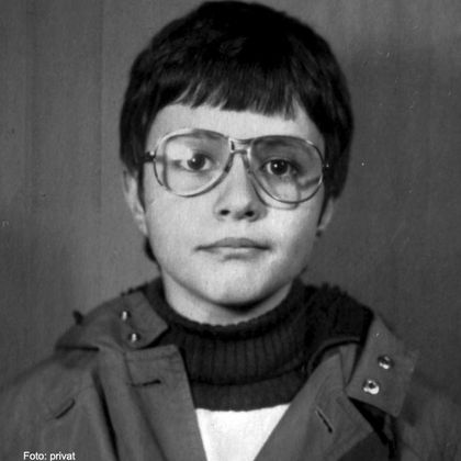 Ein schwarz-weißes Porträt eines Kindes mit Brille. Das Kind trägt eine Jacke und hat einen neutralen Gesichtsausdruck.