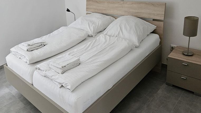 Une chambre moderne avec un lit double et du linge de lit frais. À côté du lit se trouve une table de chevet avec une lampe.