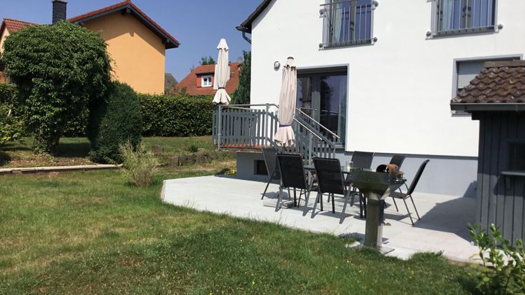 A modern house with a beautiful garden. There are garden furniture and a grill on the terrace.