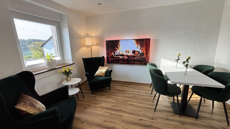 Gezellige cafe ruimte met tafels van verschillende groottes en comfortabele stoelen naast een groot raam.