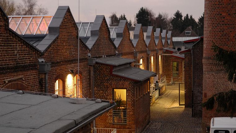 A narrow alley with brick buildings that are arranged symmetrically. The lights in the windows give the scene a cozy evening character.