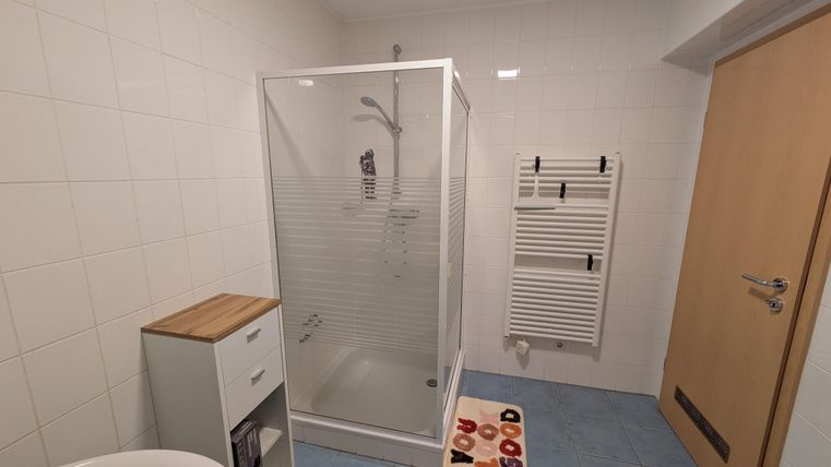 Een moderne badkamer met een douchecabine en een wastafel. De vloer is blauw betegeld, en aan de muur hangt een handdoekradiator.