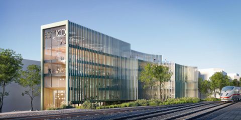 Ein modernes Gebäude mit Glasfassade und begrünten Flächen. Im Vordergrund sind Schienen für Züge zu sehen.