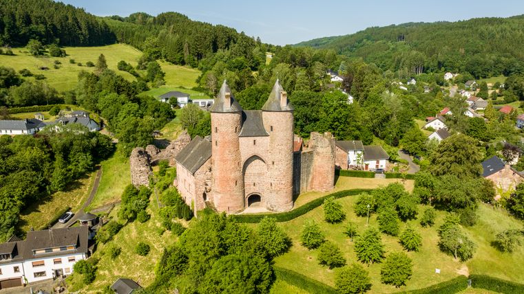 Vue aérienne du château de Bertrada à Mürlenbach, entouré d'un paysage verdoyant et de maisons.