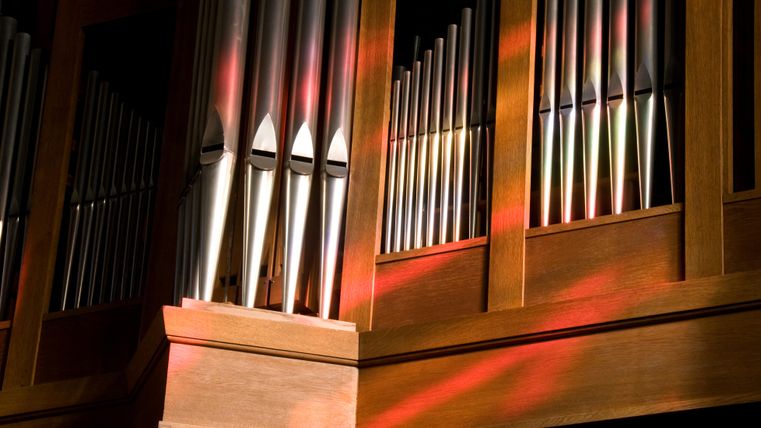 Eine Orgel mit glänzenden Metallpfeifen und warmem Holz. Sanftes Licht fällt auf die Oberfläche und erzeugt schöne Farben.