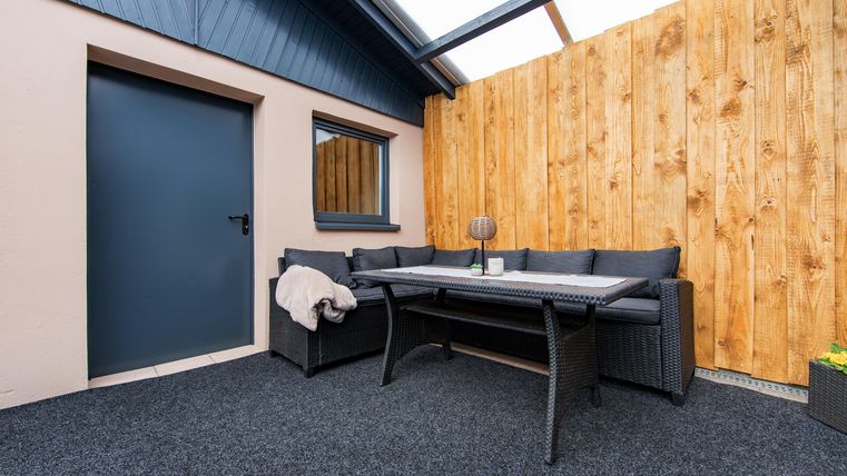 A cozy outdoor area with a modern seating group and a table. A wooden wall provides privacy and protection.