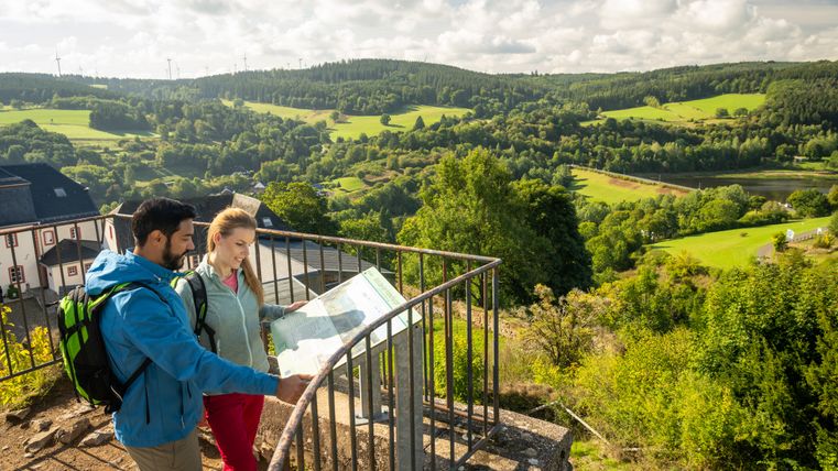 Deux personnes regardent une carte sur une plate-forme d'observation avec vue sur un paysage verdoyant.