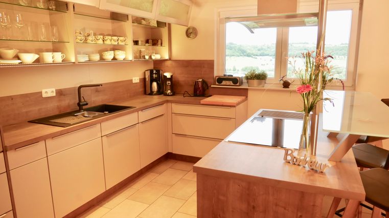 Een moderne keukenopstelling met lichte kasten en een kookgedeelte. Grote ramen zorgen voor veel daglicht en zicht op de buitenwereld.