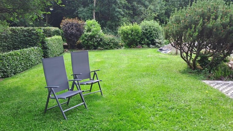 A well-kept garden with green grass and two folding chairs. In the background, bushes and trees can be seen.