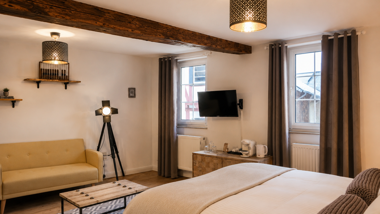 Een moderne kamer met een groot bed en een gezellige zithoek. Heldere kleuren en stijlvolle lampen zorgen voor een uitnodigende sfeer.