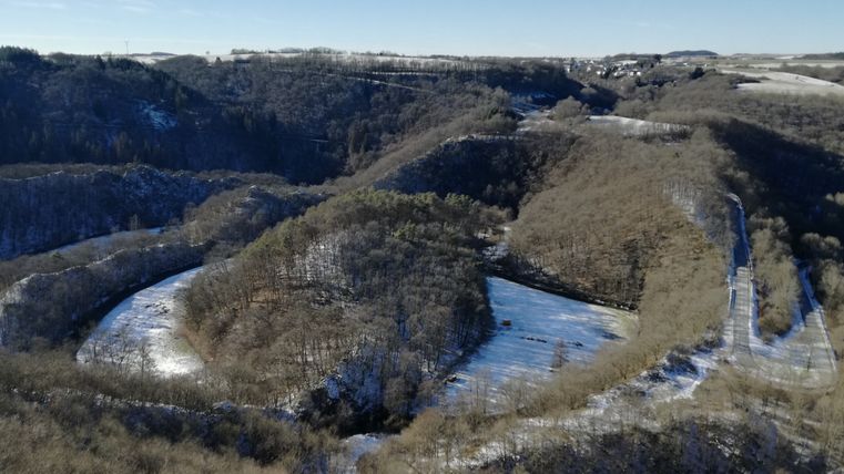 Winterlandschaft mit Fluss und Hügeln, teilweise schneebedeckt.